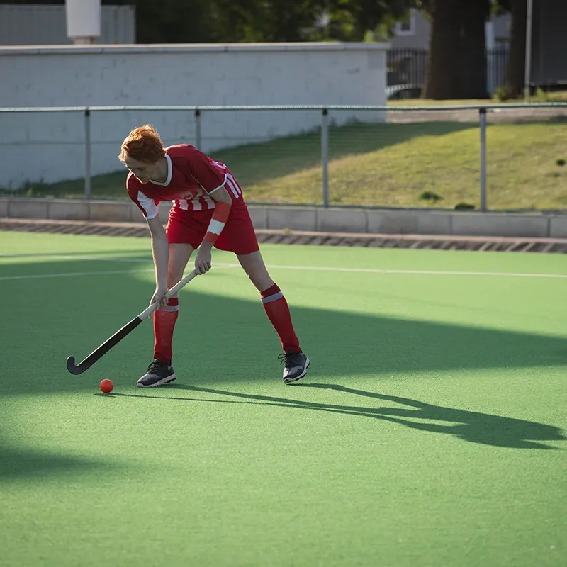 Un joueur de hockey sur gazon en tenue rouge contrôle une balle orange sur un terrain vert.